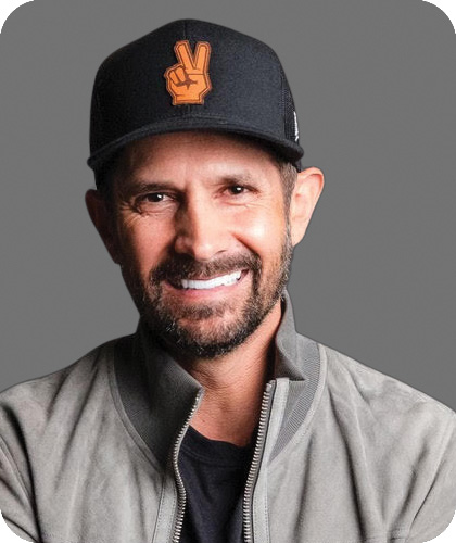 Pace Morby is wearing a black baseball hat with two fingers in a peace sign and a gray sweater, and smiling at the camera